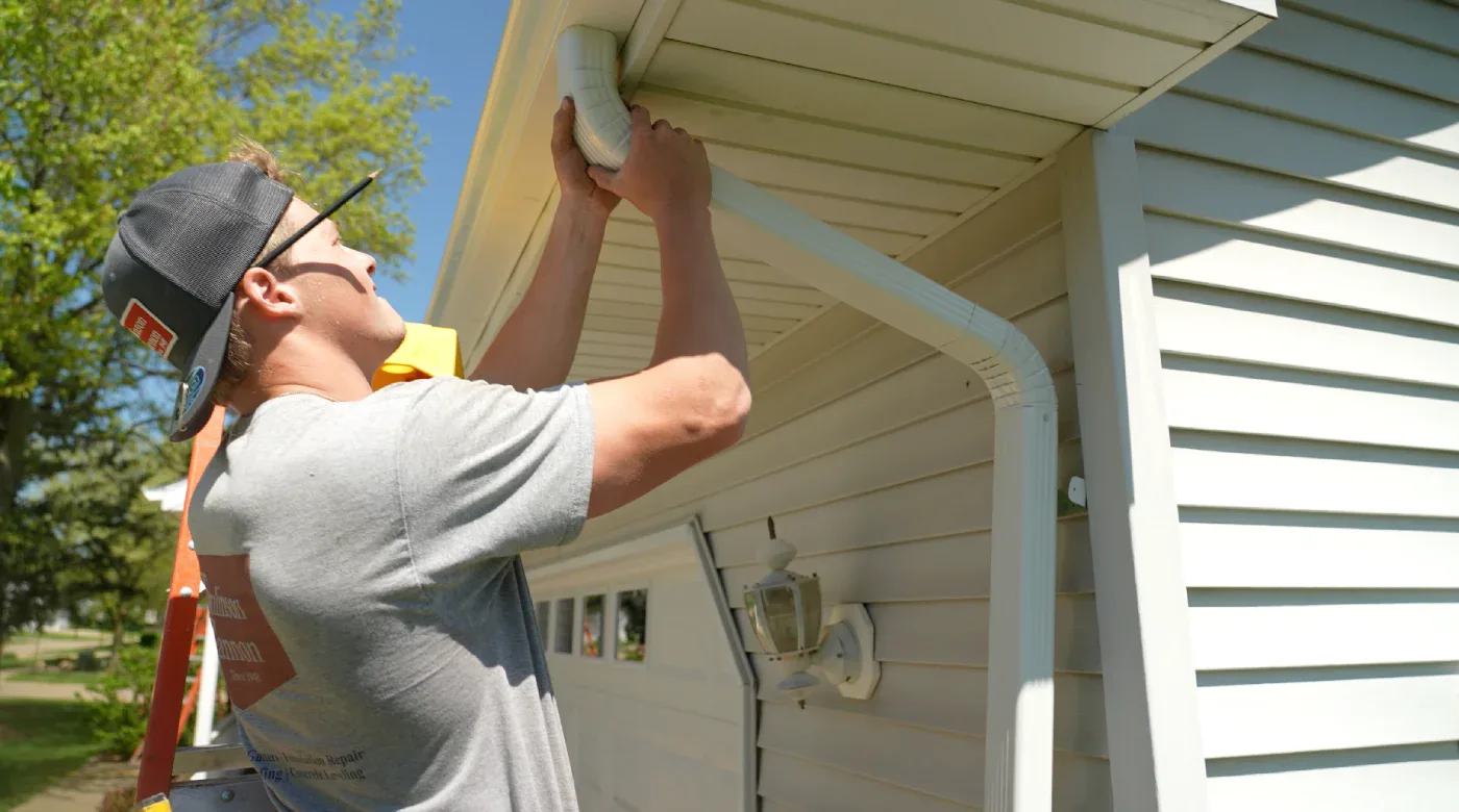 Tomlinson Cannon professional working on a residential gutter system, helping Iowa homeowners understand the differences between 5 inch vs 6 inch gutters.
